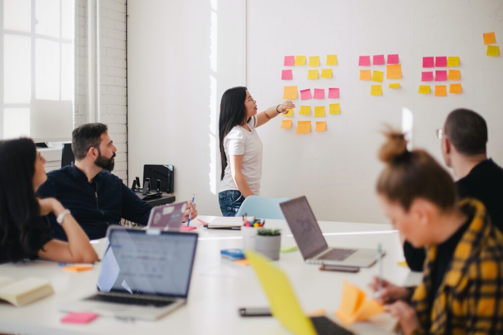 Team of professionals in a collaborative workshop practicing Agile Change Management, with one member organizing colorful sticky notes on a whiteboard, symbolising idea generation and task planning.