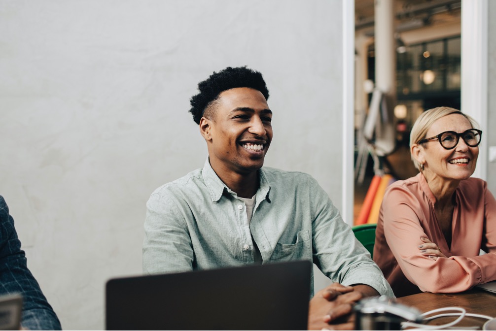 Change Delivery Partners. An image of two professional diverse consultants, one male and one female, smiling and looking towards another person not showing in the image.