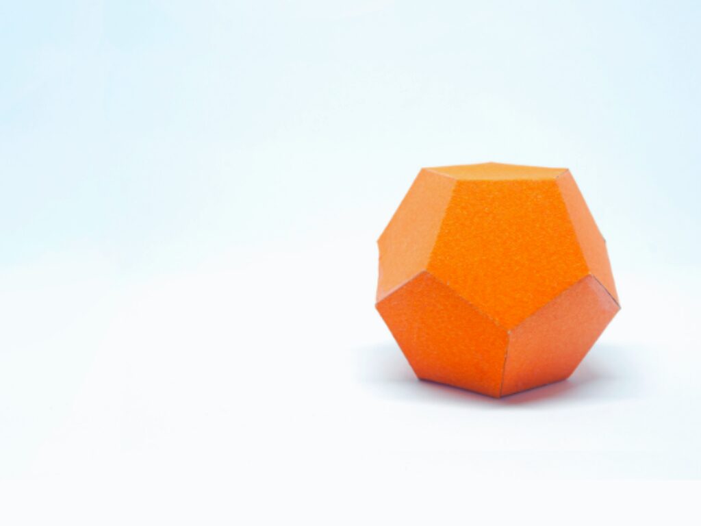 A simple image of an orange dodecahedron on a plain white background. The geometric shape, with its flat polygonal faces and sharp edges, provides a minimalist yet striking visual contrast against the soft, uniform backdrop
