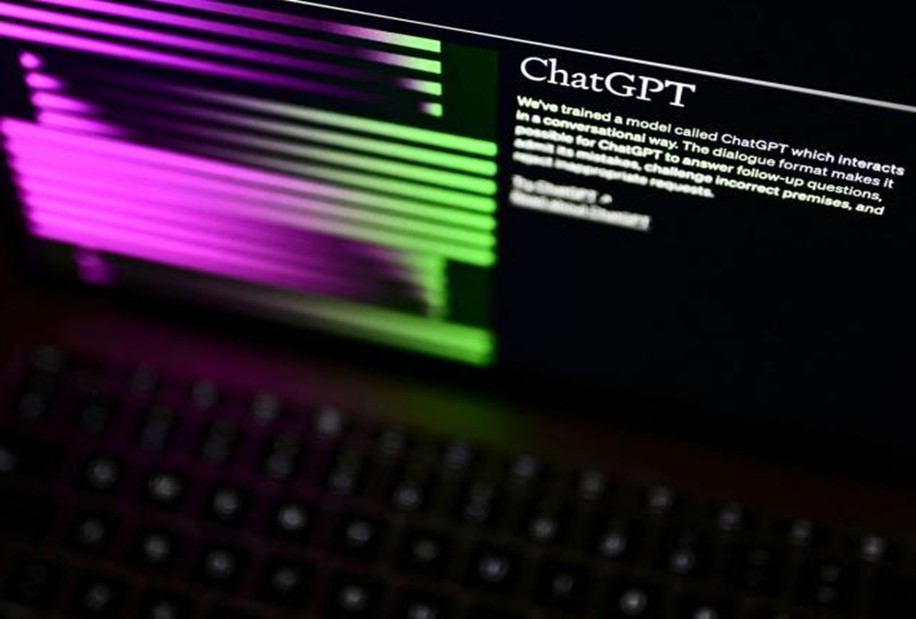 Close-up view of a computer monitor displaying text about ChatGPT, a conversational model developed by OpenAI. The screen is partially illuminated by vibrant pink and green light reflecting off a nearby keyboard. The focus is on the text 'ChatGPT' on the monitor, with the background and keyboard slightly blurred