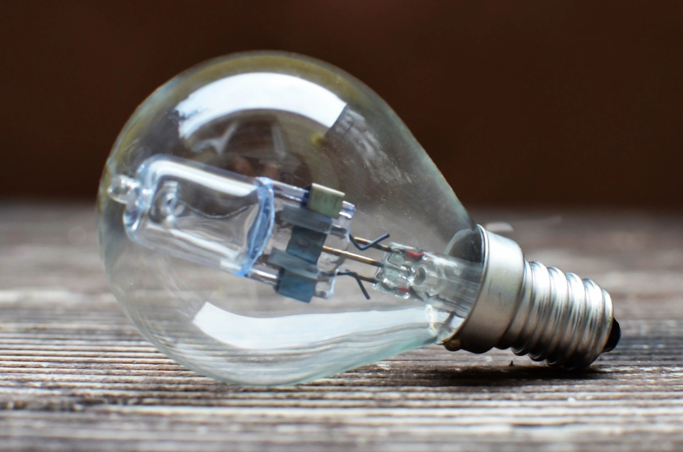 A light bulb lying on its side. The bulb is clear, revealing its inner components. This type of light bulb looks similar to a halogen bulb, which is known for being energy-efficient and providing bright light.