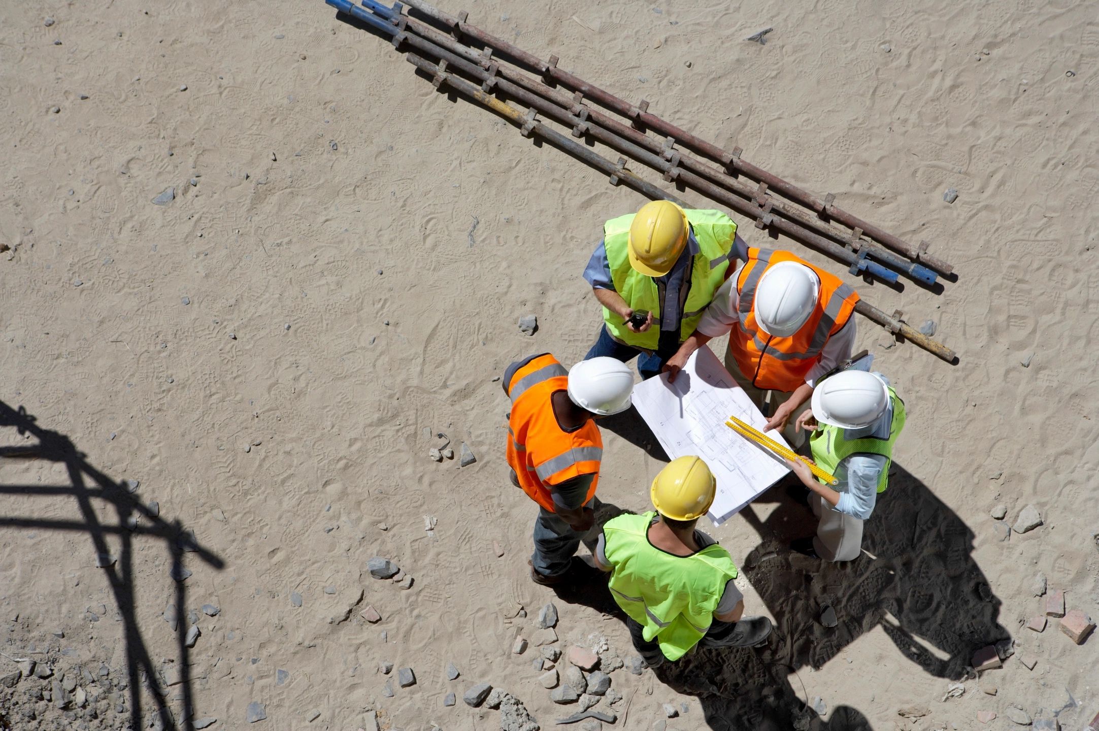 Group of construction workers in safety gear reviewing blueprints on a construction site, symbolizing the construction sector