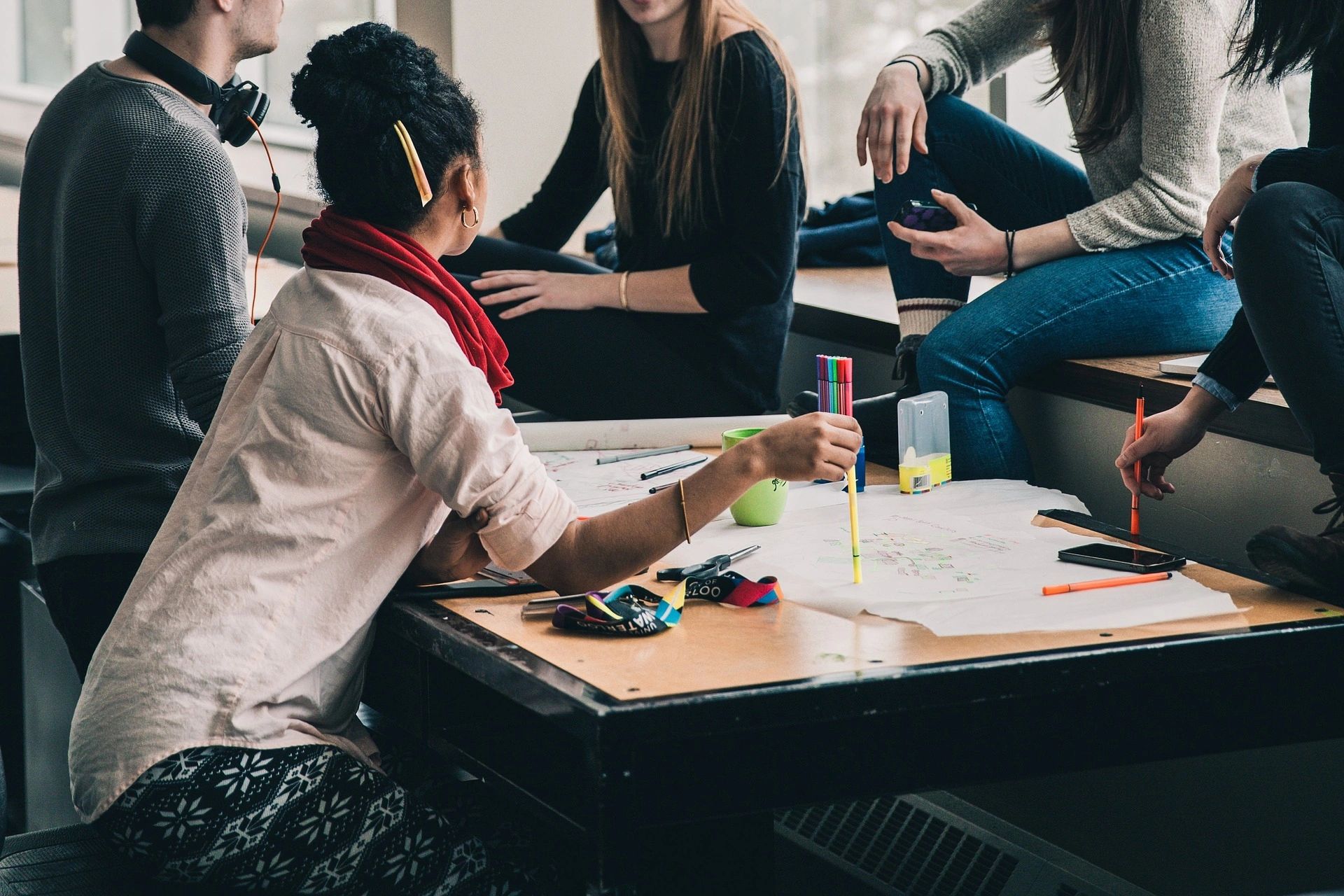 A diverse group of young professionals collaborating around a table with papers and pens, engaged in a brainstorming session. The atmosphere is casual and relaxed, suggesting a creative and productive team meeting.