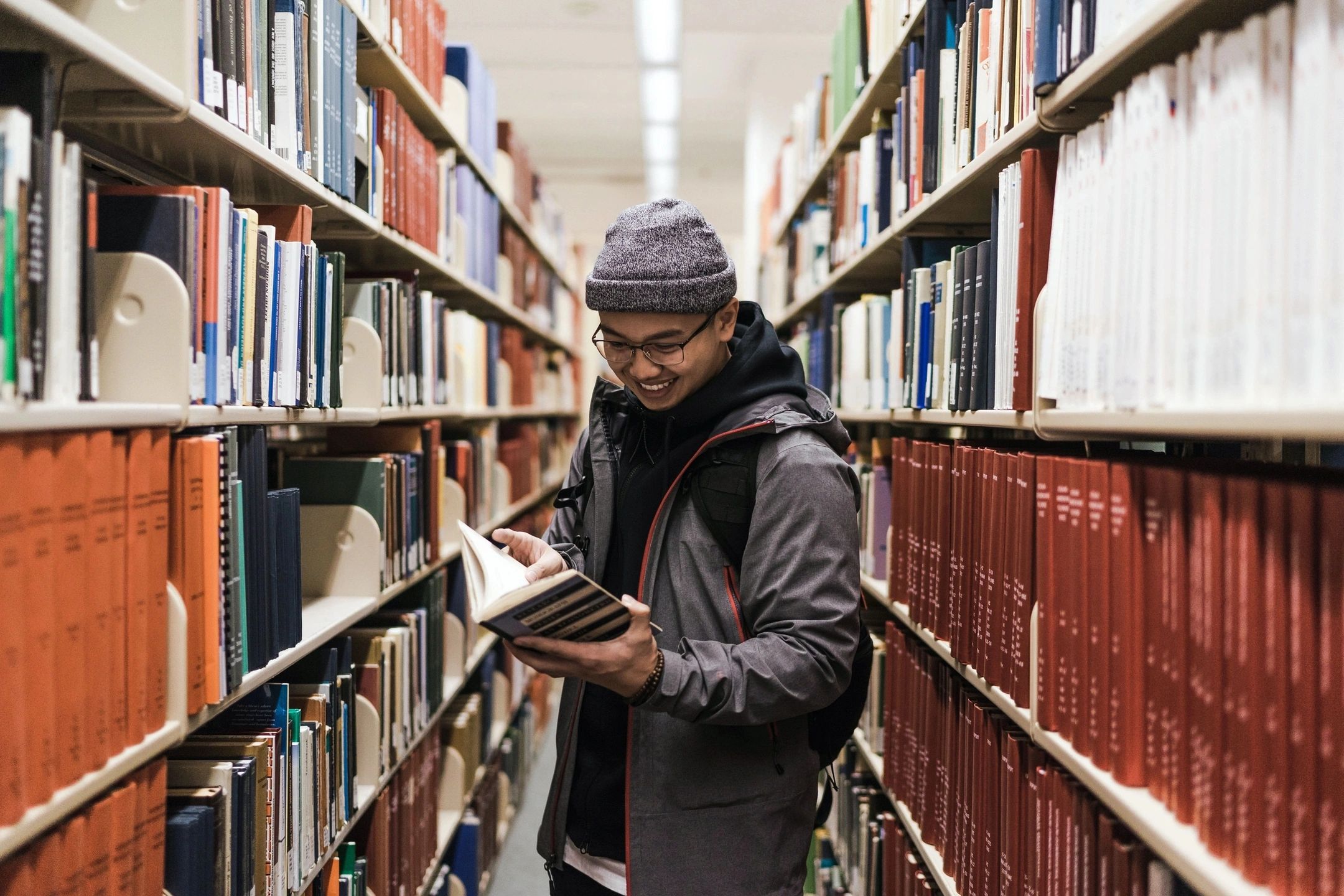Student reading a book in a library aisle, representing the education sector