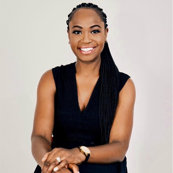 On the Meet the team page, this is a professional woman with a warm smile is seated, wearing a sleeveless black dress. Her hair is styled in long braids, swept to one side. She has a watch on her wrist and rests her hands lightly on her lap against a plain white background. The overall tone of the image conveys confidence and approachability.