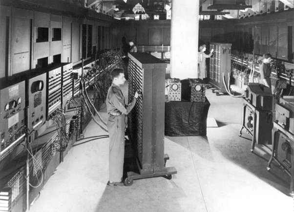 A historical black-and-white image of early computer technology, depicting engineers working on the ENIAC, one of the first electronic general-purpose computers. This moment marks a key milestone in the evolution of computing, laying the foundation for modern AI adoption in the workplace.