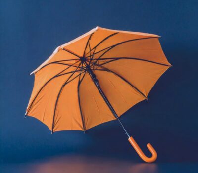 An open orange umbrella contrasts with a deep blue background, representing the concepts of protection, coverage, and inclusivity. This image metaphorically illustrates our consultancy's commitment to Business Transformation and Racial Equity, emphasising a thorough and encompassing approach