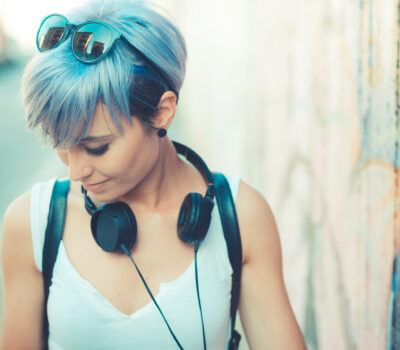 Stylish individual with blue hair, embodying urban chic and personal expression, enjoying music against a backdrop of vibrant street art, resonating with the dynamic energy of Business Transformation and Racial Equity.